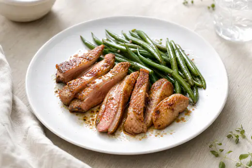 Aiguillettes de canard dorées et rosées à l’intérieur, tranchées, servies sur une assiette avec des haricots verts et un peu de sauce