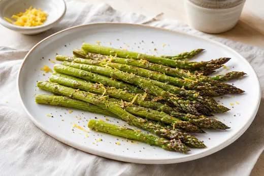 Asperges vertes rôties, les pointes dorées, posées sur une assiette avec du zeste de citron et du poivre