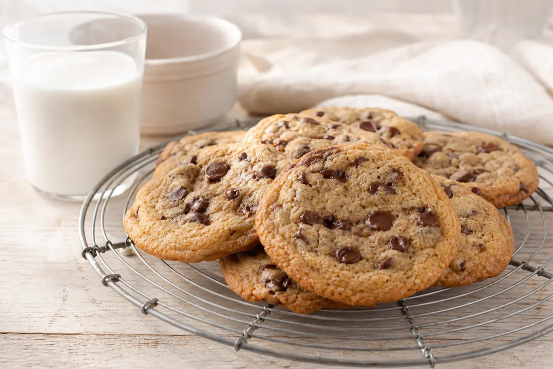 Biscuits ronds aux pépites de chocolat, dorés avec des bords croustillants, empilés sur une grille avec un verre de lait à côté