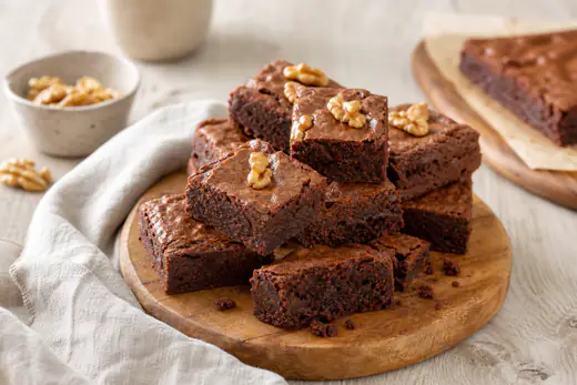 Carrés de brownie au chocolat à la croûte craquelée et au cœur fondant, avec des noix, empilés sur une planche en bois
