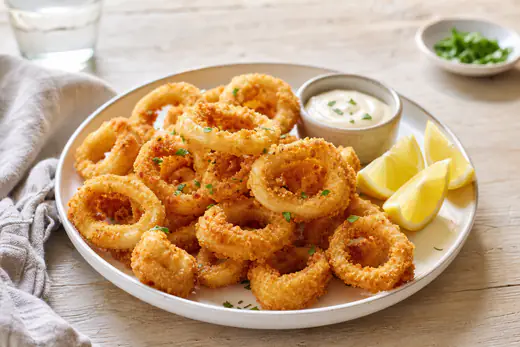 Beignets de calamars dorés et croustillants dans une assiette, avec des quartiers de citron et une petite coupelle de sauce aïoli