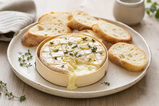 Un camembert rôti dans sa boîte en bois, coulant au centre, piqué d’ail et de thym, avec des tranches de baguette grillée autour