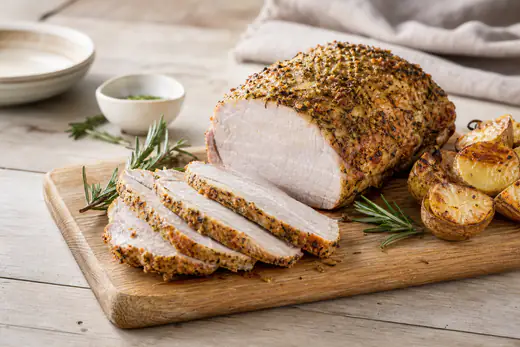 Carré de porc rôti doré, tranché en épaisses tranches sur une planche avec du romarin et des pommes de terre