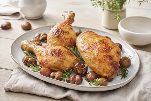 Deux cuisses et un suprême de chapon rôtis à la peau dorée, posés sur un plat avec du romarin et des marrons