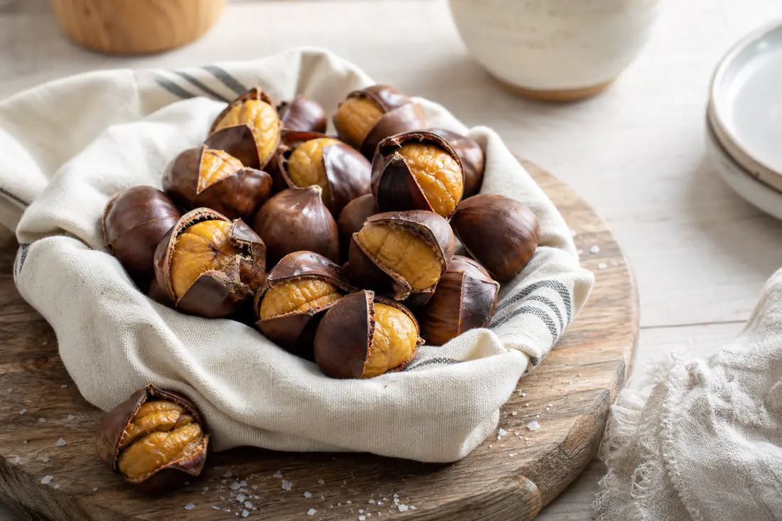Châtaignes grillées dont la peau brune est fendue, laissant voir la chair dorée, servies dans un torchon sur une planche en bois