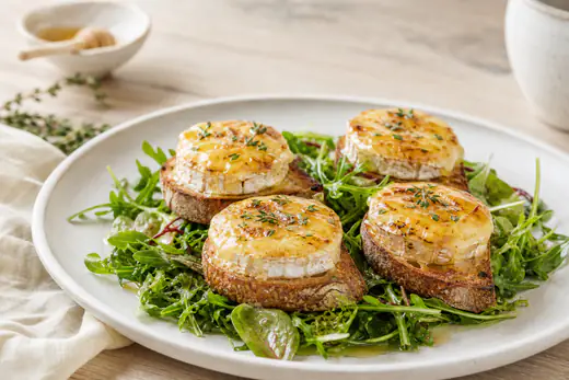Quatre toasts de chèvre chaud dorés au miel et au thym, servis sur une assiette avec une salade verte et une vinaigrette