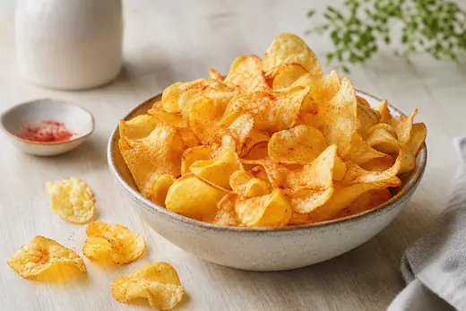 Un grand bol de chips de pommes de terre maison très fines, dorées et ondulées, avec une pincée de paprika fumé