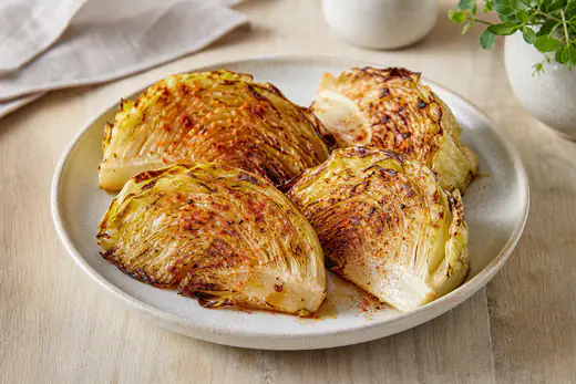 Quartiers de chou blanc rôtis, aux bords dorés et caramélisés, saupoudrés de paprika fumé et servis sur une assiette