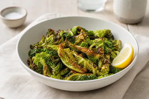Lanières de chou frisé vert rôties, aux bords croustillants et bruns, dans un bol avec un quartier de citron