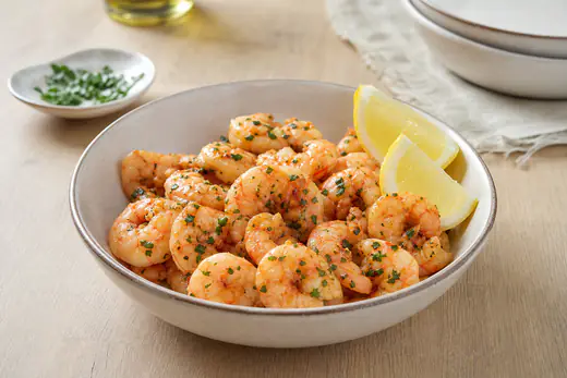 Crevettes roses saisies à l’ail et au paprika, servies dans un bol avec du persil frais et des quartiers de citron
