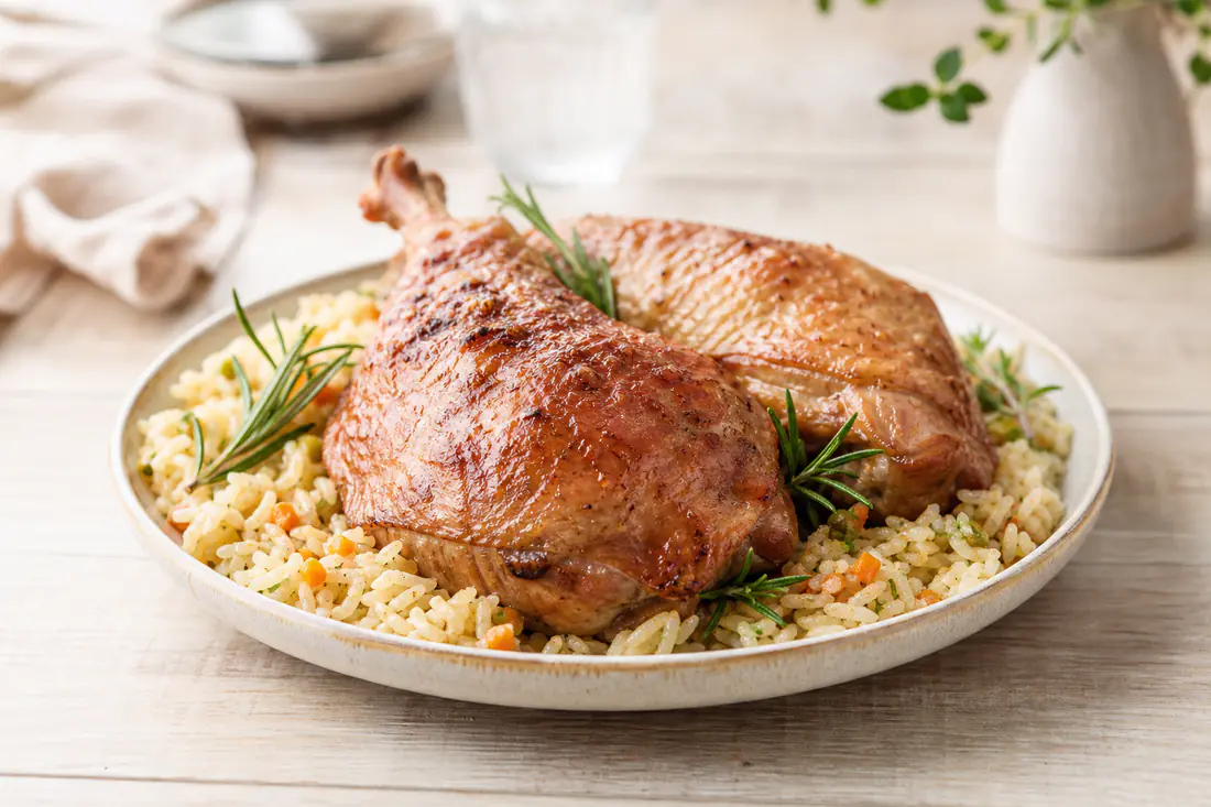 Deux cuisses de dinde à la peau dorée et croustillante, posées sur une assiette avec du riz pilaf et des brins de romarin