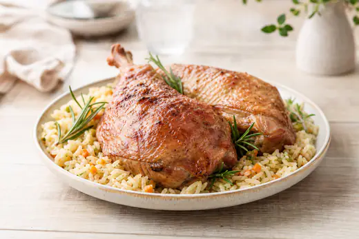 Deux cuisses de dinde à la peau dorée et croustillante, posées sur une assiette avec du riz pilaf et des brins de romarin