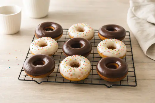 Donuts ronds en forme d’anneau avec un trou au centre, nappés d’un glaçage blanc et de vermicelles colorés, posés sur une grille