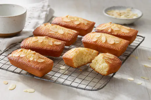 Huit financiers rectangulaires dorés aux amandes posés sur une grille, un financier coupé en deux montrant une mie moelleuse