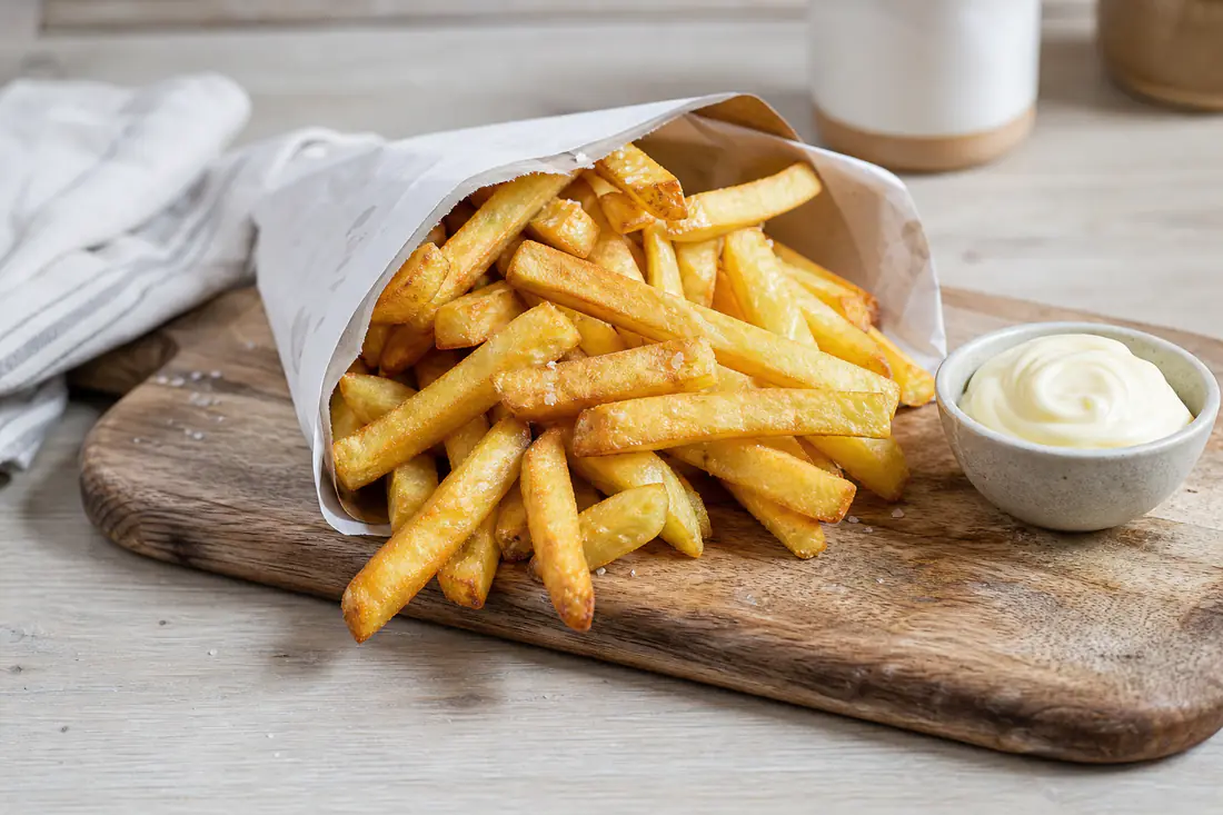 Une grande portion de frites maison dorées et croustillantes, salées et servies dans un cornet en papier avec un petit bol de mayonnaise