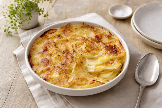 Petit gratin dauphinois doré dans un plat rond en céramique, rondelles de pommes de terre visibles sur le bord, avec une cuillère