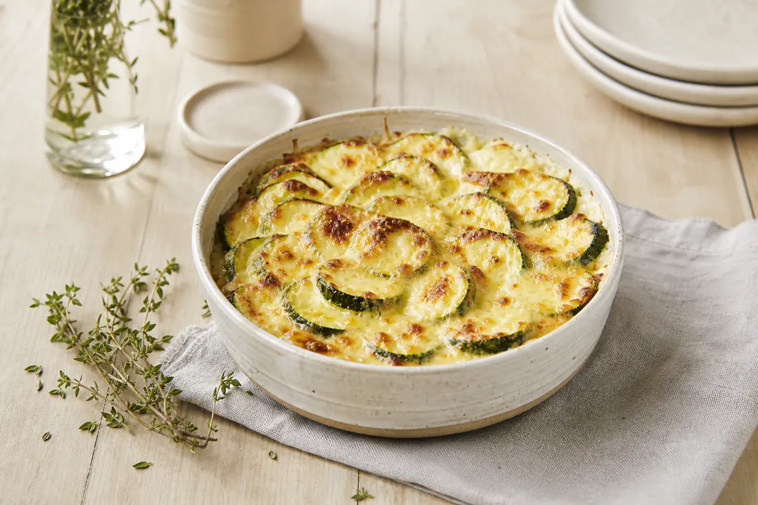 Gratin de courgettes doré dans un petit plat rond, rondelles de courgettes visibles sous une croûte de gruyère gratiné