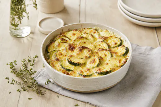 Gratin de courgettes doré dans un petit plat rond, rondelles de courgettes visibles sous une croûte de gruyère gratiné