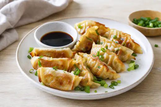 Gyozas dorés et croustillants disposés dans une assiette, avec un bol de sauce soja au vinaigre et de la ciboule émincée