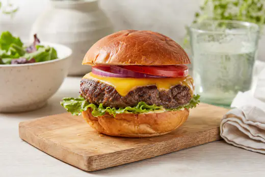 Hamburger maison avec un steak haché épais, cheddar fondu, salade, tomate et oignon rouge dans un pain grillé, posé sur une planche en bois
