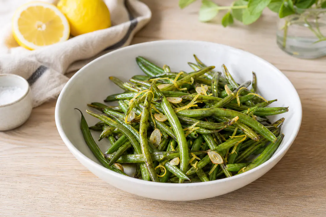 Un bol de haricots verts fins rôtis, légèrement dorés aux extrémités, relevés de zeste de citron et d’ail