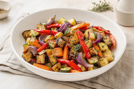 Mélange de légumes grillés avec poivron rouge, courgette, aubergine, carottes et oignon rouge, dorés aux bords, dans un plat blanc