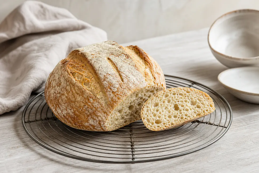 Petite boule de pain maison à la croûte dorée et farinée, entaillée de trois traits, posée sur une grille de refroidissement