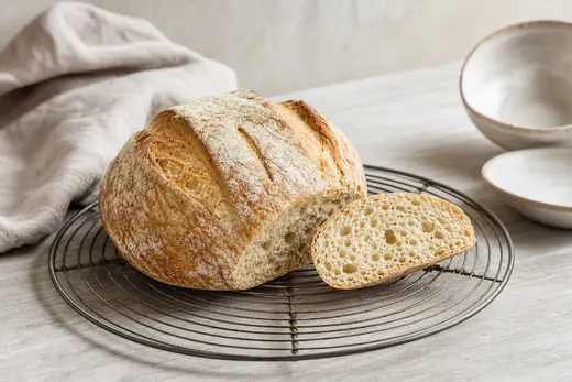 Petite boule de pain maison à la croûte dorée et farinée, entaillée de trois traits, posée sur une grille de refroidissement