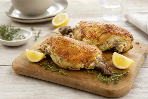 Deux poitrines de poulet avec la peau dorée et croustillante, posées sur une planche avec des quartiers de citron et du thym