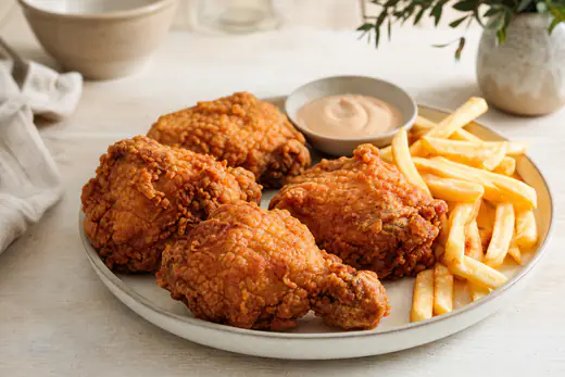 Quatre hauts de cuisse de poulet frit à la croûte dorée et craquante, servis avec des frites et une sauce