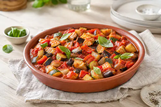 Ratatouille de cubes d’aubergine, courgette, poivron et oignon dans une sauce tomate, avec du basilic, dans un plat en terre cuite