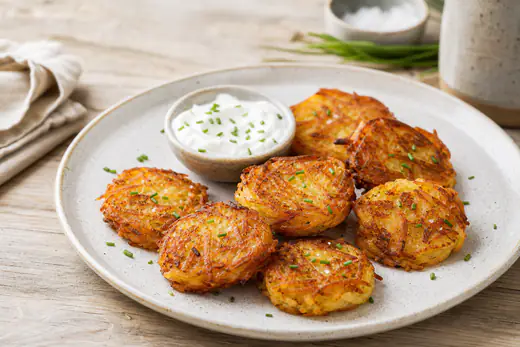 Plusieurs petites galettes de rösti dorées et croustillantes sur une assiette, servies avec de la crème fraîche et de la ciboulette