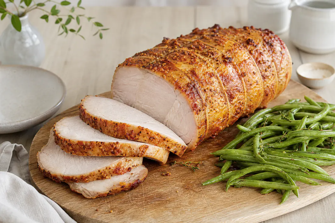 Rôti de porc ficelé à la croûte dorée, tranché en tranches épaisses et juteuses, servi avec des haricots verts