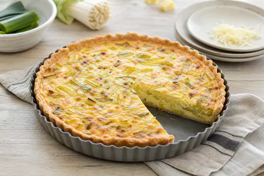 Petite tarte salée ronde aux poireaux et au gruyère, croûte dorée, coupée en parts dans son moule en métal