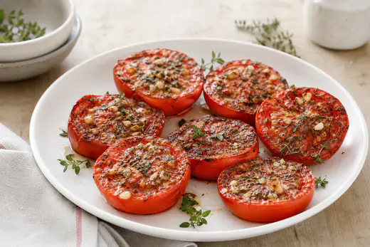 Moitiés de tomates grillées, la chair fondante et légèrement dorée, avec des herbes de Provence et de l’ail, sur une assiette