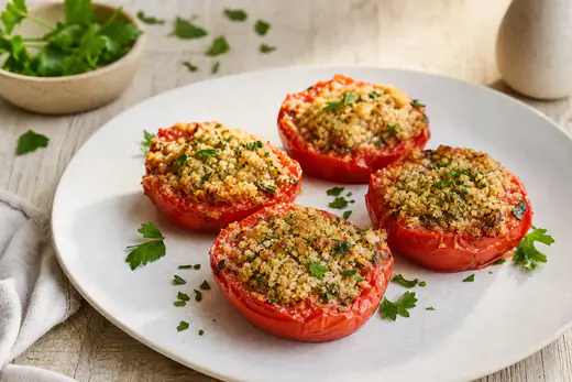 Moitiés de tomates à la provençale recouvertes d’une persillade dorée à l’ail et au persil, sur une assiette blanche